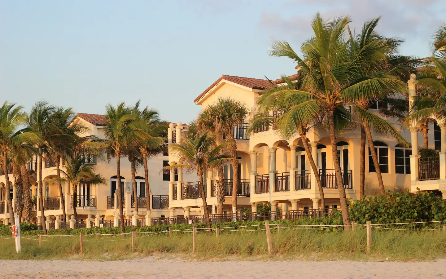 Edificios de condominios frente a la playa detrás de dunas y palmeras